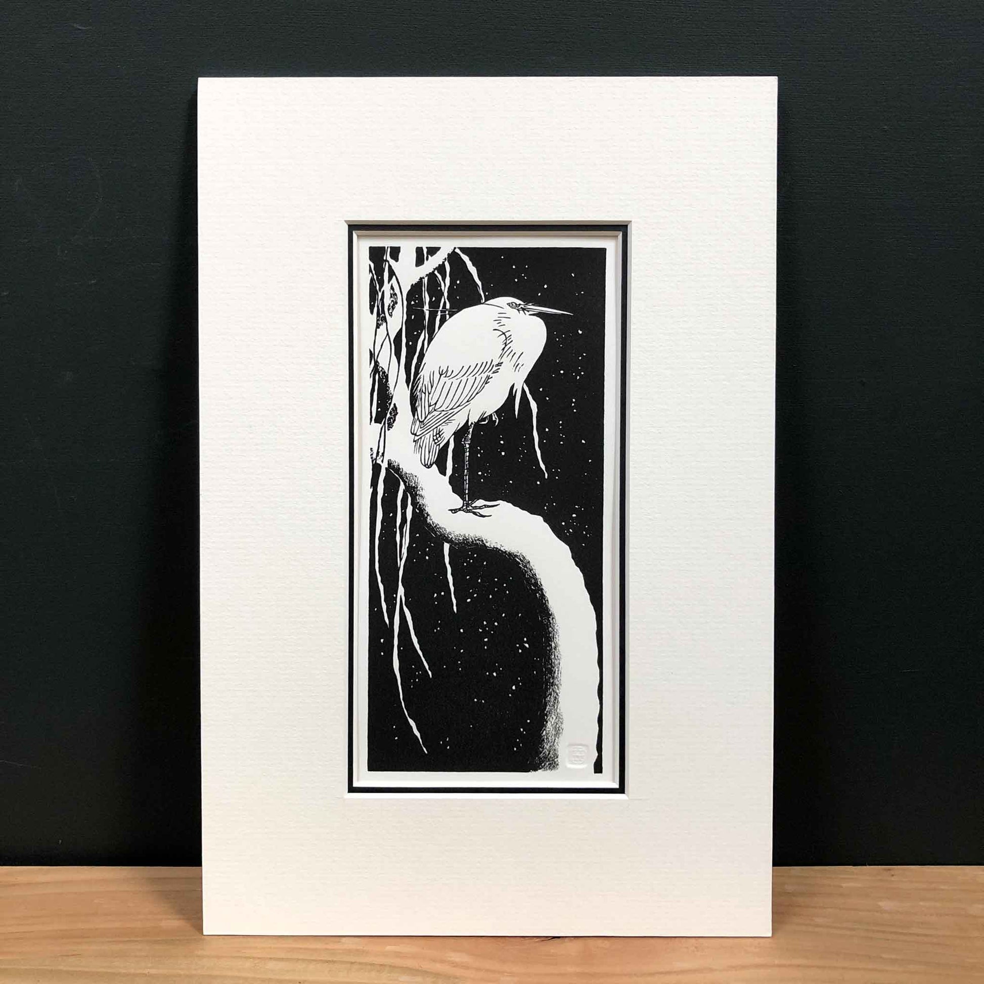 Egret on a Snow-Covered Branch, after Koson — handmade woodblock print by Claire Cameron-Smith, mounted in soft cream board, displayed against dark wall