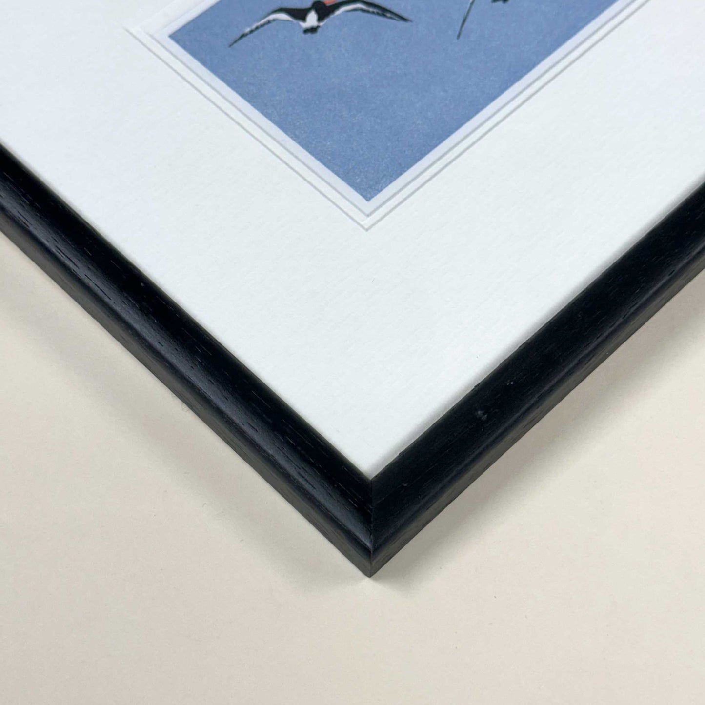 Handmade print of Oyster Catchers in Flight against blue background - close up of black frame.