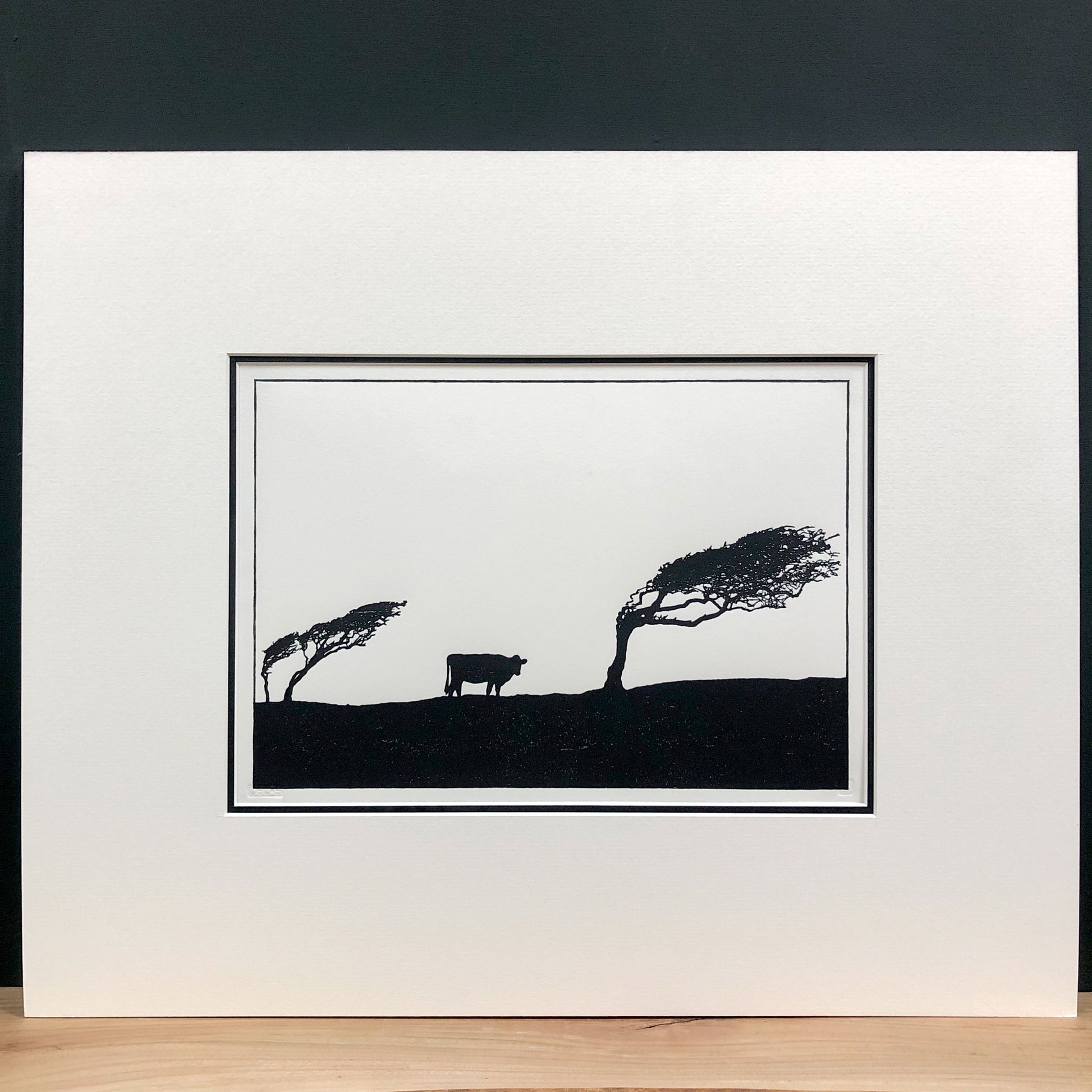 Original handmade woodblock tree print of windswept hawthorns and cow in black ink on cream paper, fourth print in a series of four, mounted with wide cream mount and black inner mount.